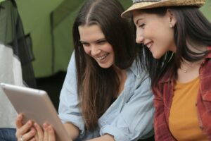 Two women laughing together while watching a tablet, showcasing friendship and happiness.